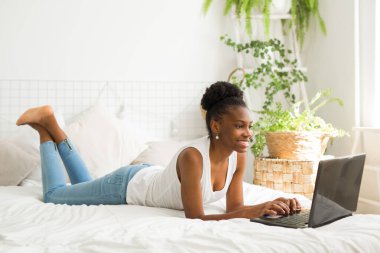  Güzel, genç bir Afrikalı kadın dizüstü bilgisayarla yatakta yatıyor.