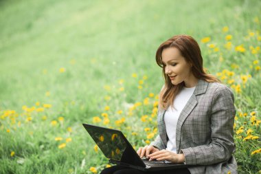 Parkta dizüstü bilgisayarı olan gri ceketli güzel bir kadın.