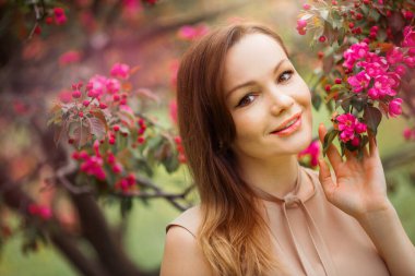 Çiçekli bir ağacın yanında makyajlı güzel bir kadının portresi.