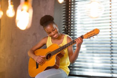 Gitar çalan güzel, genç bir Afrikalı kadın.