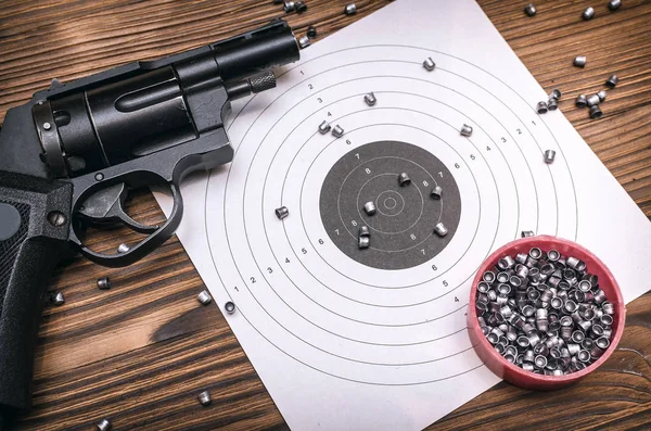 Gun pistol and paper target with scattered bullets around. Shooting practice. Shooting range background with copy space.