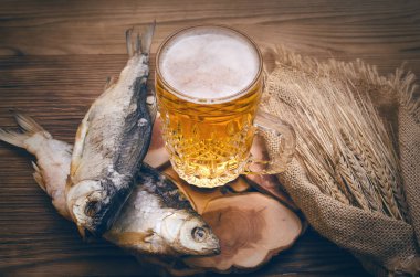 Köpük bira bir bardağa, çuval bezi yanık ahşap masa arka plan üzerinde sarılı balık stockfish ve çavdar kulakları kurutulmuş.