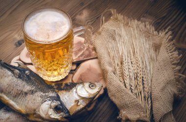 Köpük bira bir bardağa, çuval bezi yanık ahşap masa arka plan üzerinde sarılı balık stockfish ve çavdar kulakları kurutulmuş.