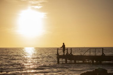 Bayahibe 6 'da gün batımında iskelede bir balıkçı.