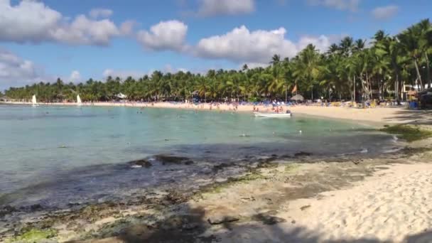 View of Dominicus beach in Bayahibe in Dominican Republic during the morning with the sun, with boats on the sea and palm trees and tourists populating the beach 2 — Stock Footage View Dominicus Beach Bayahibe Dominican Republic Morning Sun Boats Sea Royalty Free Stock Footage