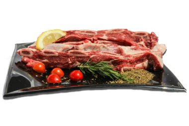 Beyaz arka planda çiğ et ve yiyecek süslemeleri olan tenha bir tabak.