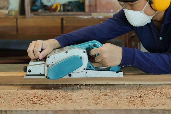 Tischler mit elektrischer Hobelmaschine mit Holzplanke in Tischlerei. er trägt Sicherheitsausrüstung — Stockfoto