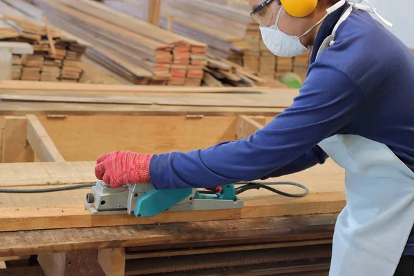 Tukang kayu menggunakan papan listrik dengan papan kayu di bengkel kayu. Dia memakai peralatan keselamatan. — Stok Foto