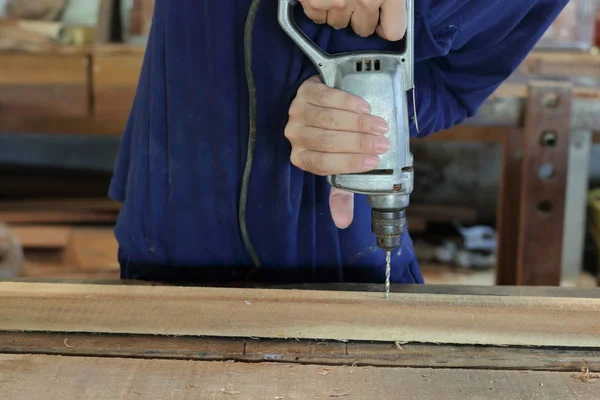 Mano de trabajador perfora un agujero con tablón de madera utilizando la máquina de perforación eléctrica en el taller —  Fotos de Stock
