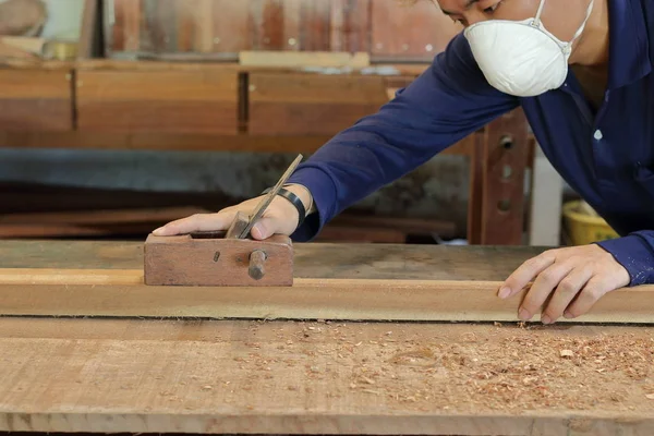 Carpinteiro trabalhando com uma plaina de mão em uma prancha de madeira em oficina de carpintaria. Está a usar equipamento de segurança.  . — Fotografia de Stock