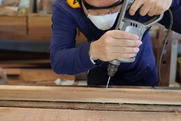 Trabalhador faz um buraco usando máquina de perfuração elétrica na oficina de carpintaria. Está a usar equipamento de segurança.  . — Fotografia de Stock