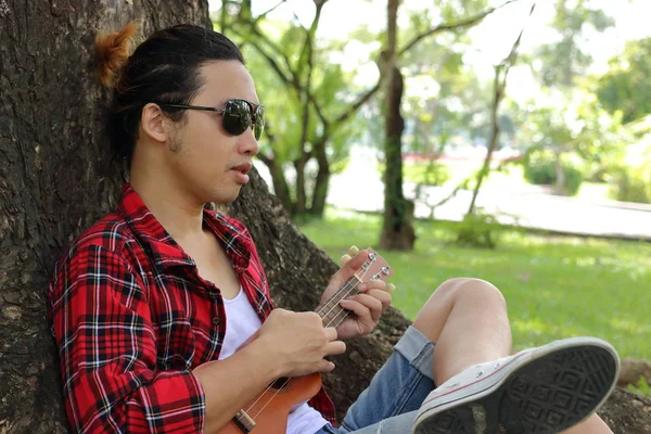 Ukulele açık park karşı rahatlatıcı genç hipster adamdır.
