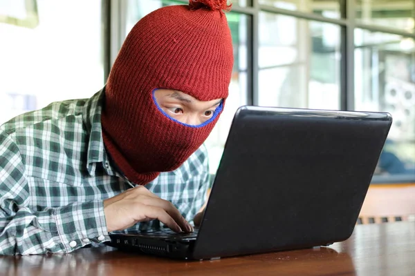 Masked hacker wearing a balaclava stealing data from laptop. Internet security concept. — Stock Photo, Image