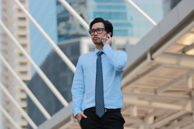 Yakışıklı genç Asyalı işadamı cep telefonu şehir arka plan yaptığı iş konuşurken.