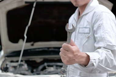 Profesyonel genç makinist adam araba İngiliz anahtarıyla garaj arka plan açık kukuleta tutan eller yukarı kapatın. Oto Tamir Servisi.