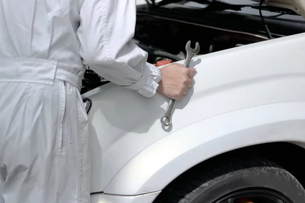 Side view of automotive mechanic in uniform with wrench diagnosing engine under hood of car at the repair garage. — Stock Photo, Image