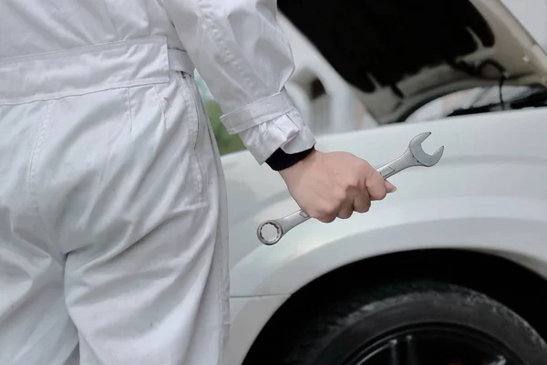 Selective focus on hands of professional mechanic man holding wrench with car in open hood at the repair garage background. — Stock Photo, Image