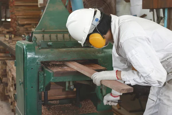 Seitenansicht eines jungen Holzarbeiters in weißer Schutzuniform bei der Arbeit mit Hobelmaschine in der Fabrik. — Stockfoto