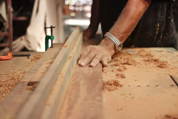 Enfoque selectivo y profundidad de campo superficial. Vista frontal de un trozo de madera se está afeitando en una mesa de enrutador por manos de carpintero en taller de carpintería . —  Fotos de Stock