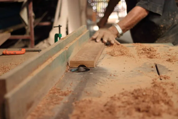 Enfoque selectivo y profundidad de campo superficial. Un trozo de madera está siendo afeitado en una mesa de enrutador por manos de carpintero en taller de carpintería . —  Fotos de Stock