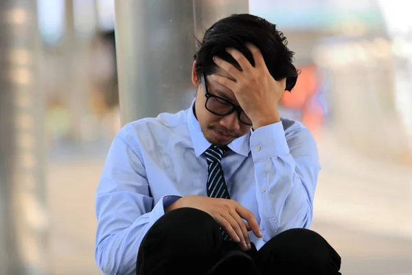 Nahaufnahme eines gestressten jungen asiatischen Geschäftsmannes mit der Hand auf der Stirn, der auf dem Boden sitzt. Erschöpfung und Kopfschmerzen im Job. — Stockfoto