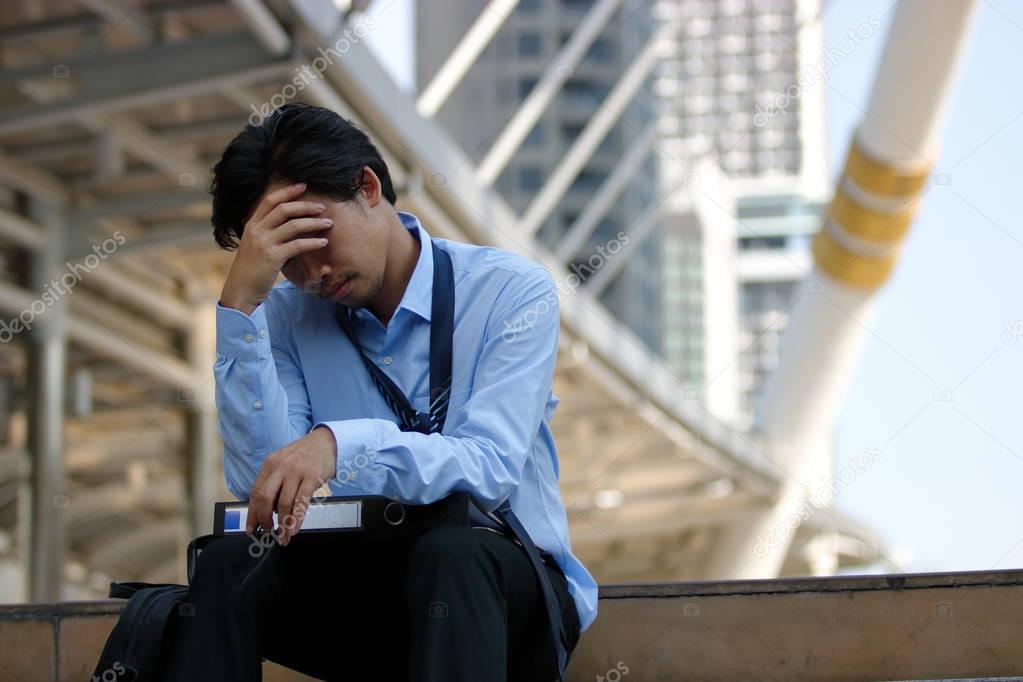 Frustrated stressed Asian businessman with hand on forehead sitting on staircase in the city. Depressed unemployment business concept.