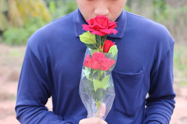 A beautiful bouquet of artificial red roses is held by young relaxed man on nature blurred background. Love and romance concept. — Stock Photo, Image