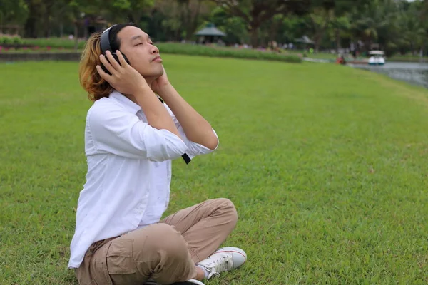 Портрет молодого чоловіка, який відпочиває з навушниками в парку на відкритому повітрі — стокове фото