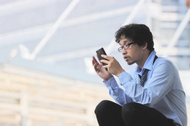 Genç işsiz Asya adam bulanık şehir arka plan mobil akıllı telefon ile iş bulma yan görünüm.