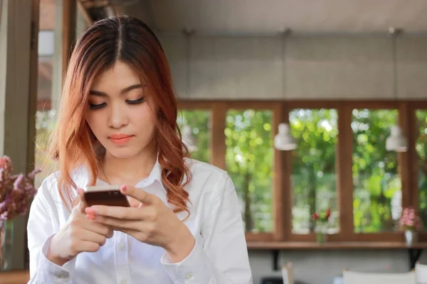 Селективный акцент на лице молодой азиатской бизнес-леди, держащей мобильный телефон в кафе . — стоковое фото