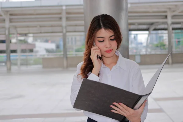 Портрет молодой привлекательной азиатской деловой женщины, говорящей по телефону о своей работе на открытом городском фоне . — стоковое фото