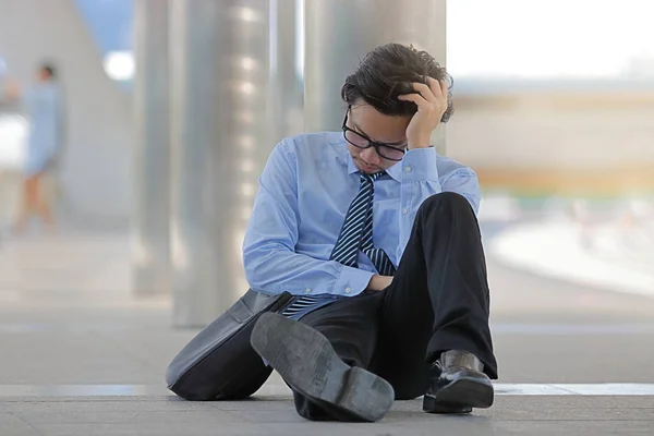 Portrait of stressed young Asian man sitting on the floor of sidewalk and feeling tired with job