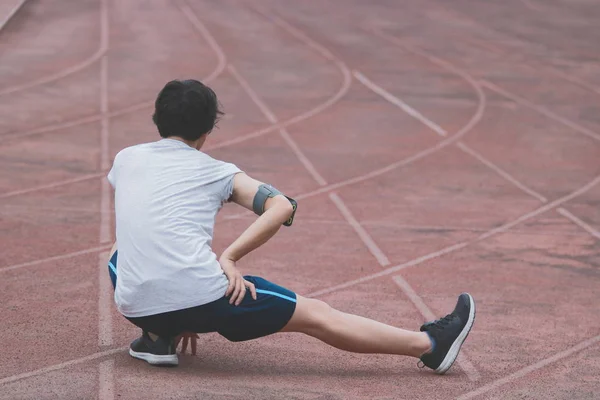 Back view of young Asian runner man warming up before run on track in the stadium