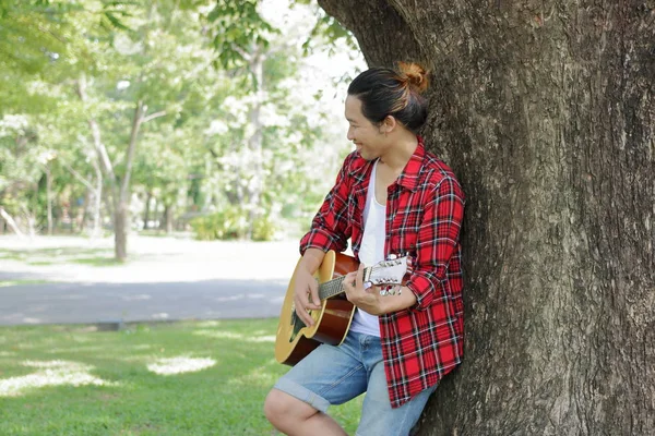 若い男は屋外の公園でアコースティック ギターを演奏に傾いています。. — ストック写真