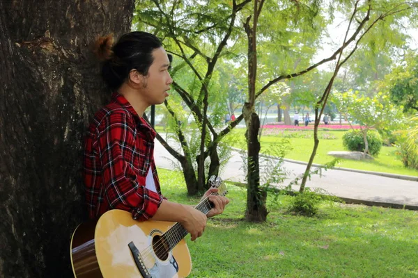 Портрет гітариста або музиканта грає на акустичній гітарі на прекрасному фоні природного парку . — стокове фото