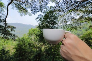 Yakın beyaz kahve fincanı kadar güzel yeşil doğa ve dağ arka planı Gezgin eller tarafından düzenlenmektedir.