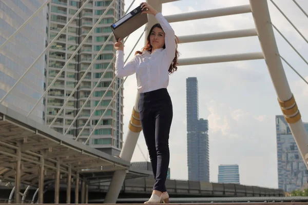 Porträtt av unga attraktiva asiatisk affärskvinna tog upp dokumentmapp för att skydda solljus i utomhus city bakgrunden. — Stockfoto
