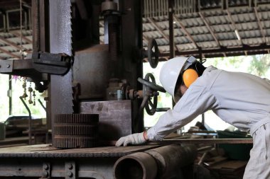 Dikey şerit testere makinesi marangozluk fabrikasında bir parça tahta kesim üniforma tekniği ve koruması aygıtları genç işçi yan görünüm.