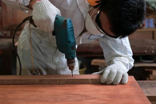 Joven trabajador asiático con taladro eléctrico de trabajo de seguridad en tablero de madera en taller de carpintería . —  Fotos de Stock