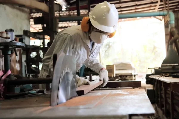 Professionelle junge Arbeiter in weißer Uniform und Sicherheitsausrüstung schneiden ein Stück Holz auf Tischsäge Maschine in Tischlerei Fabrik. — Stockfoto