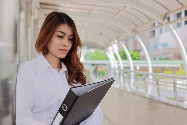 Портрет молодой привлекательной азиатской предпринимательницы, держащей папку с документами на пути к внешнему офису с копировальным пространством . — стоковое фото