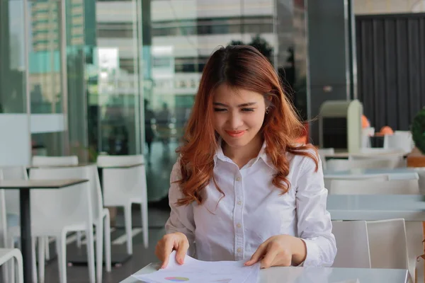 Портрет счастливой молодой деловой женщины, сидящей и держащей в руках бумажную работу или графики против улыбки его работы в офисе . — стоковое фото