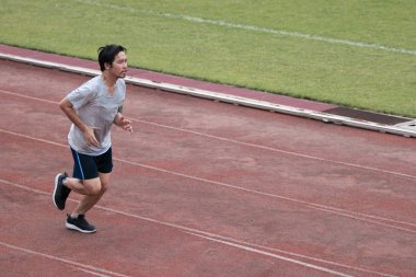 Yakışıklı sporcu Asya Stadyumu kopya alan arka plan ile yarış pisti üzerinde koşan adam. Sağlıklı aktif yaşam tarzı kavramı.