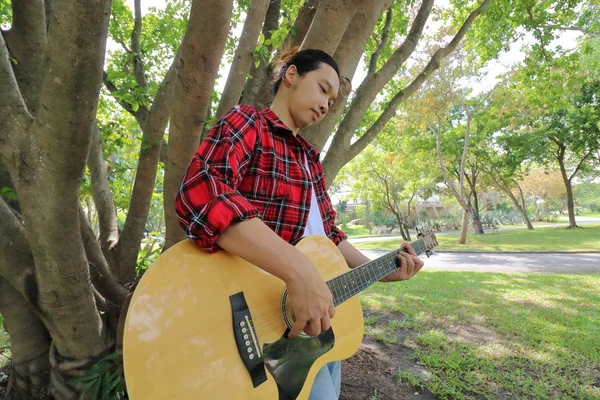 Amplo ângulo tiro de belo jovem tocando música na guitarra acústica em um belo fundo natureza . — Fotografia de Stock
