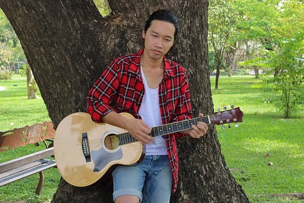 Молодий красивий чоловік грає музику на акустичній гітарі в парку . — стокове фото