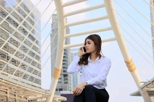 Porträtt av unga attraktiva asiatisk affärskvinna talar på smart mobiltelefon i staden byggnad bakgrund. — Stockfoto