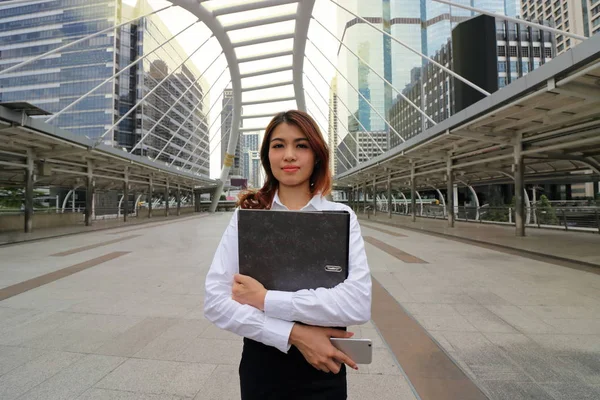 Porträtt av unga attraktiva asiatiska företag kvinna stå och hålla dokumentmapp på city bakgrunden. — Stockfoto