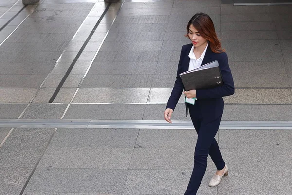 Vista aérea de la joven atractiva mujer de negocios asiática sosteniendo la carpeta de documentos y caminando en el suelo de la ciudad contra el espacio de copia de fondo . — Foto de Stock