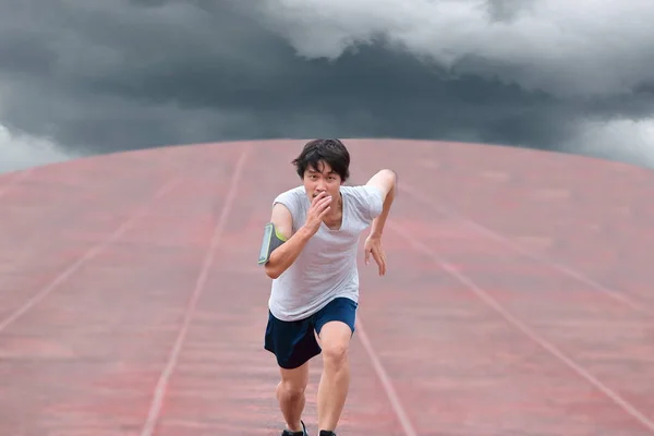 Jovem corredor asiático correndo na pista com tempestade meteorológica no céu escuro nublado fundo . — Fotografia de Stock