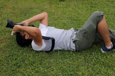 Genç fotoğrafçı yeşil çim kamera dslr elinde tutan ile yatan adam.